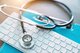 Photo of a stethoscope curled on top of a white keyboard and blue clipboard [Image by creator Witthaya from AdobeStock]